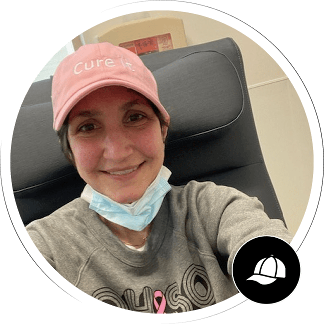 A smiling woman wearing a pink "Cure It" hat.