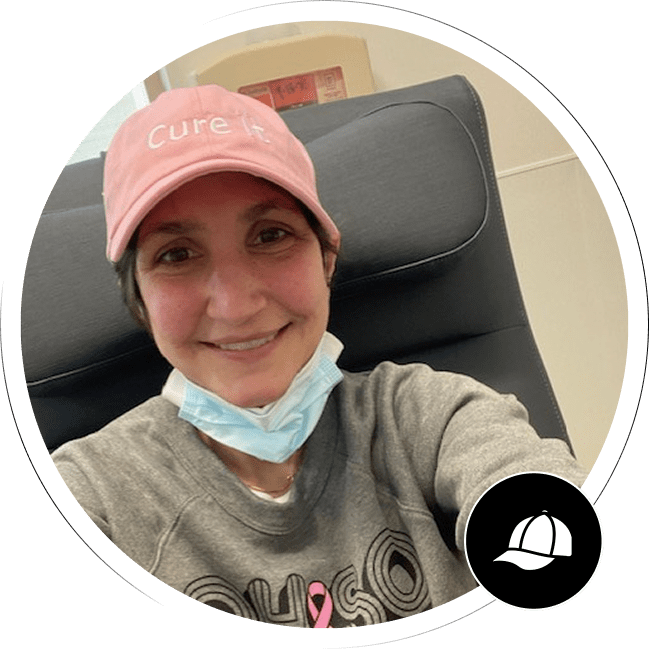 A smiling woman wearing a pink "Cure It" hat.