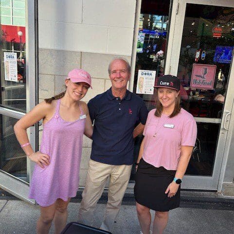 Man and two women wearing pink hats